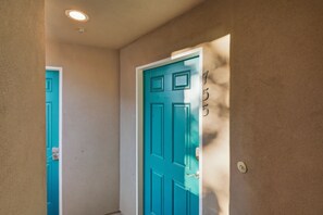 A hallway with a teal door, a white door, and a wall with a number plaque.