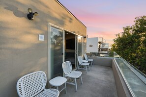 A balcony with white chairs and a glass door leading to an interior space.