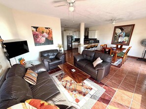 A living room with two sofas, a coffee table, and a TV. There is a kitchen in the background with a dining area. - Private House & Casita with Pool and Ocean Views (Cruz de Huanacaxtle)