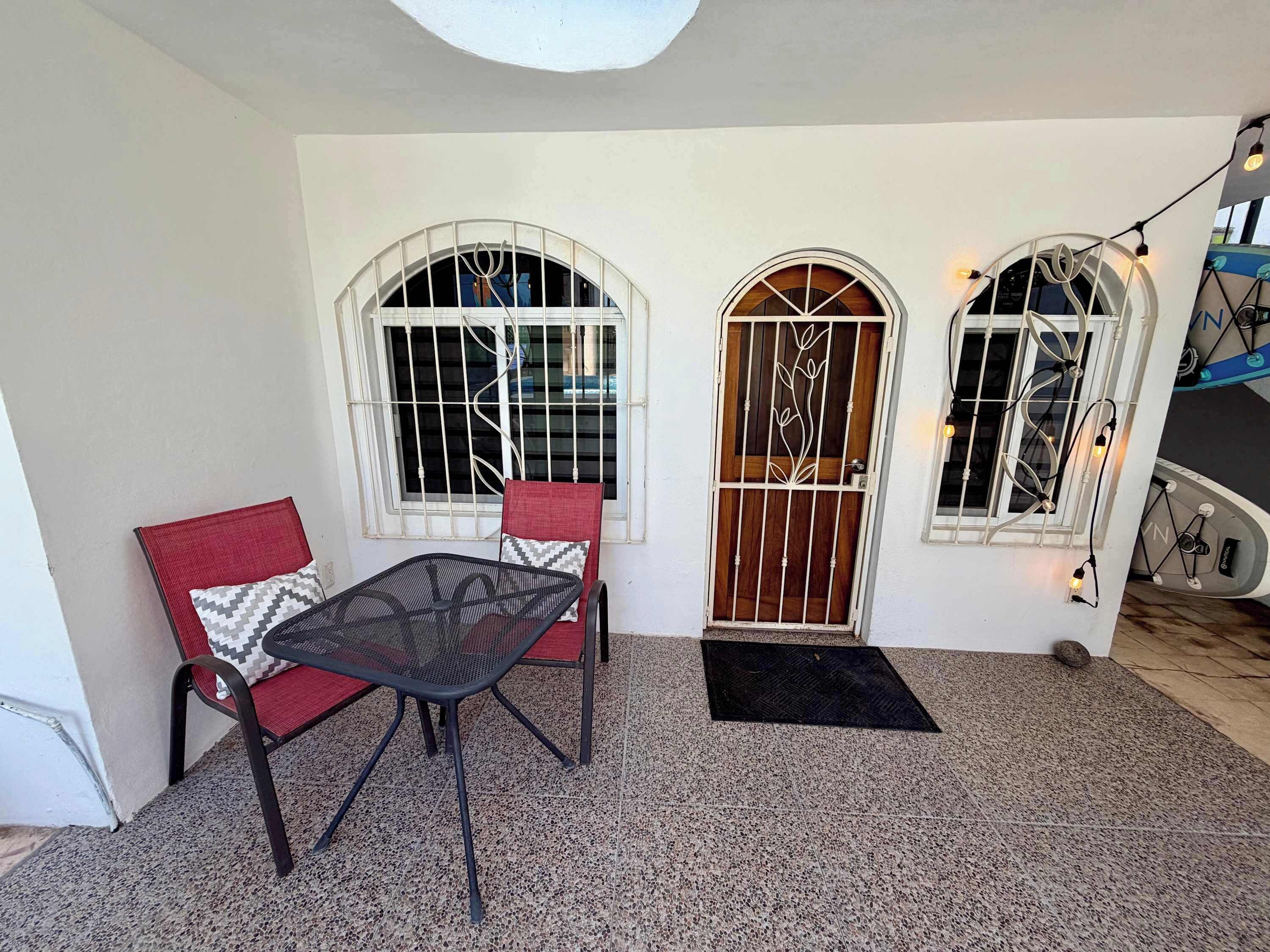 A room with a table and two chairs, a door with a metal gate, and a window with a decorative design.