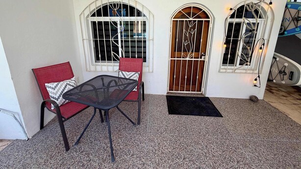 Una habitación con una mesa y dos sillas, una puerta con reja de metal y un ventanal con diseño decorativo.