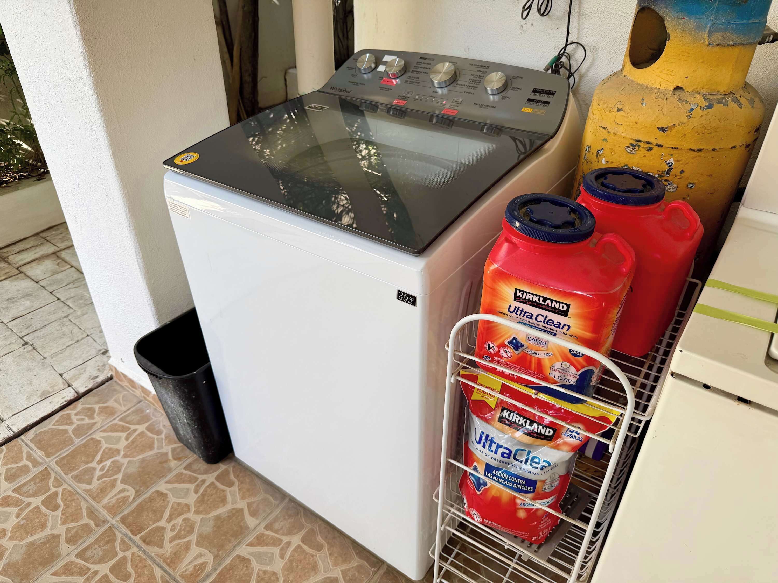 Een compacte koelkast met waterdispenser, gasfles en een plank met flessen Kirkland Ultra Clean wasmiddel.