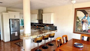 Una cocina con una isla central, taburetes de bar, una mesa de comedor y un cuadro en la pared.