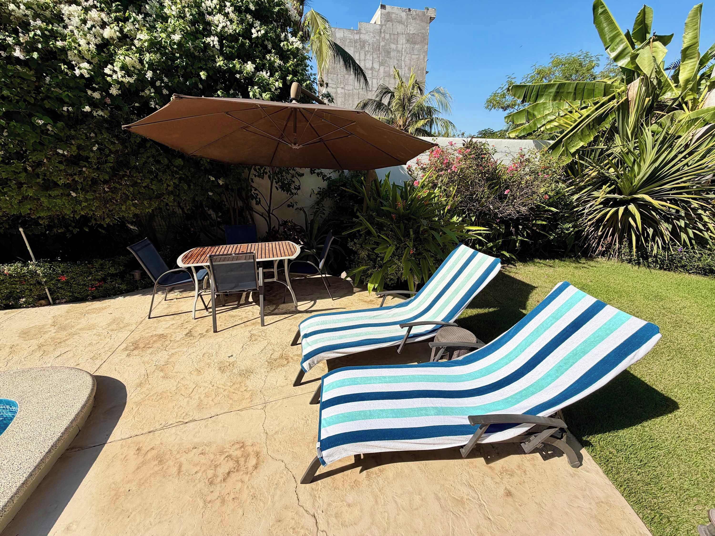 A patio with two striped lounge chairs, a table, and an umbrella.