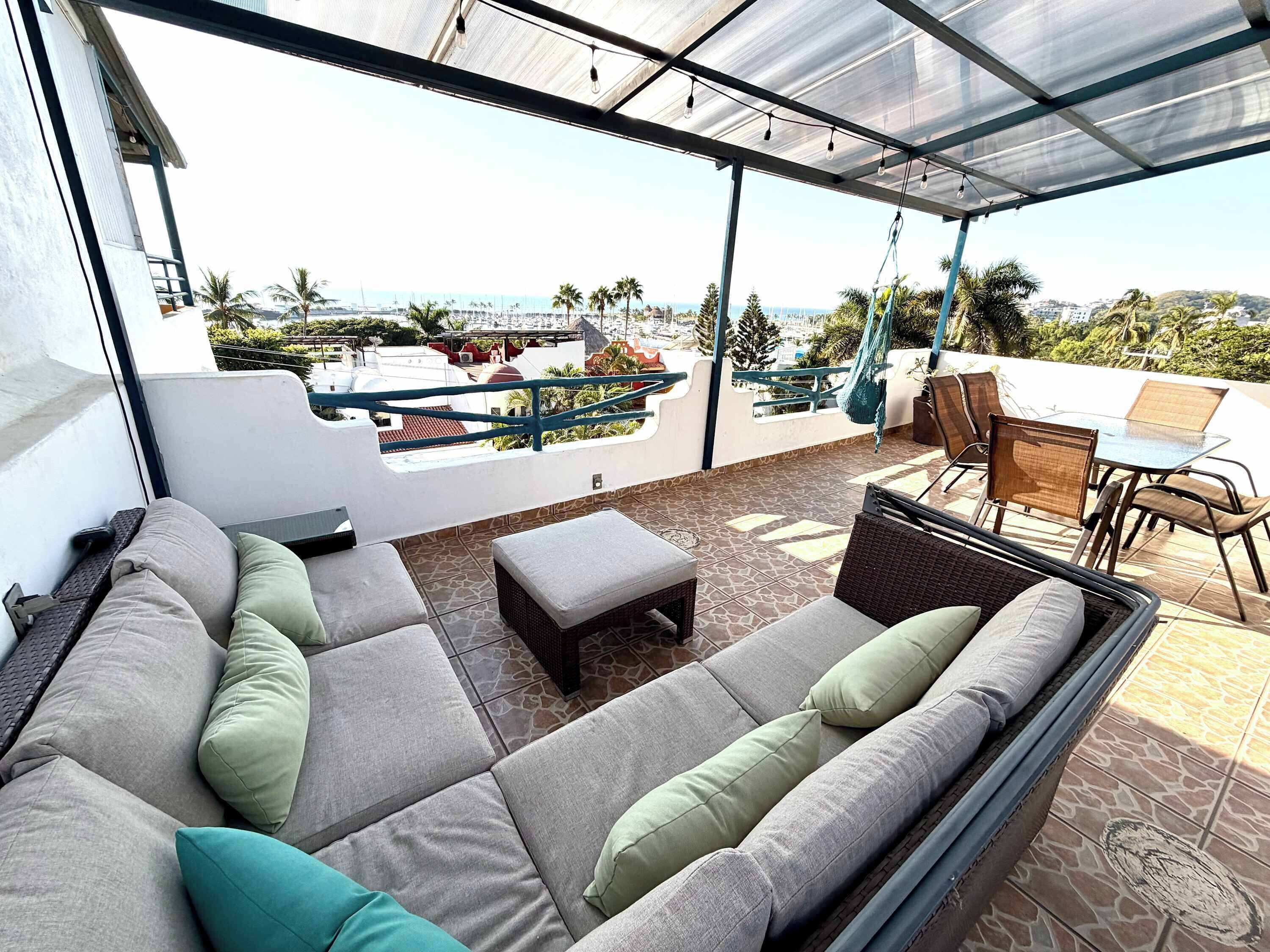 A covered outdoor seating area with a sofa and chairs, a table, and a view of the cityscape.