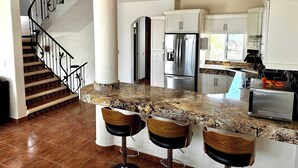Una cocina con encimera de granito, electrodomésticos de acero inoxidable y una escalera de madera.