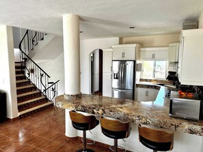 A kitchen with a granite countertop, stainless steel appliances, and a wooden staircase. - Private House & Casita with Pool and Ocean Views (Cruz de Huanacaxtle)