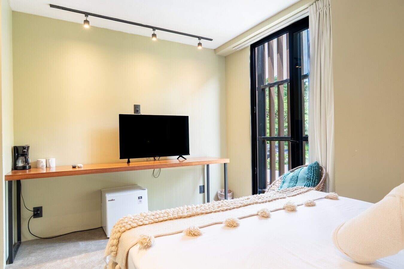 Un dormitorio con cama, televisor sobre un mueble bajo, cafetera y un pequeño electrodoméstico blanco.