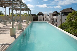 Une piscine agrémentée d’une pergola et de hamacs, entourée de bâtiments aux toits de chaume.