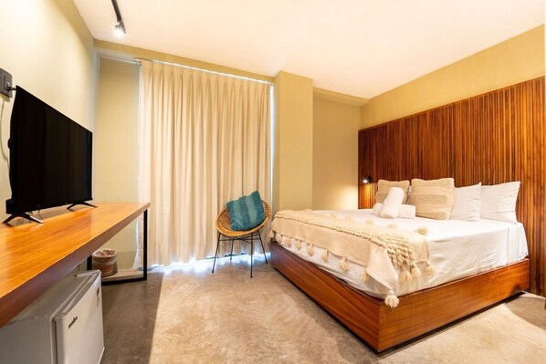 Une chambre à coucher avec un lit en bois, un téléviseur posé sur un bureau, une chaise et une fenêtre avec des rideaux.