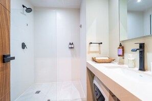Une salle de bain moderne avec une douche à parois de verre, un lavabo doté d’un distributeur de savon et un miroir au-dessus du plan de toilette.