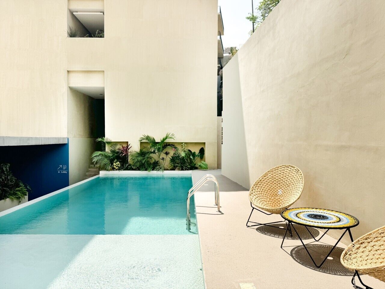A swimming pool with a metal ladder, two wicker lounge chairs, and a small garden area with plants.