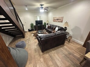 A living room with a dark leather sofa, a flat-screen TV, a coffee table, and a staircase. - Cozy 2-bedroom 2 full bath townhome in Ruston near Tech Campus! (Ruston)