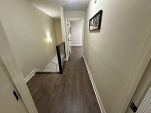 A hallway with a wooden floor, a white door at the end, and a wall-mounted light fixture. - Cozy 2-bedroom 2 full bath townhome in Ruston near Tech Campus! (Ruston)