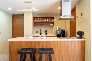 A modern kitchen with a central island, bar stools, a coffee machine, and a water dispenser. - Modern 1BR Suite | Rooftop Pool + Parking (Sayulita)