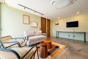 Ein modernes Wohnzimmer mit einer Couch, Sesseln, einem Couchtisch und einem an der Wand befestigten Flachbildfernseher.
