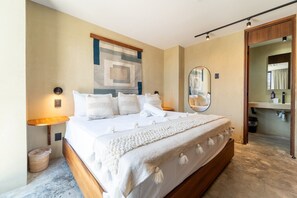 Ein Hotelzimmer mit einem großen Bett, einem Nachttisch mit Lampe, einem an der Wand befestigten Spiegel und Blick ins Badezimmer.