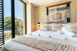 A hotel room with a large bed, a view of the outdoors, and a wall-mounted artwork. - Modern 1BR Suite | Rooftop Pool + Parking (Sayulita)