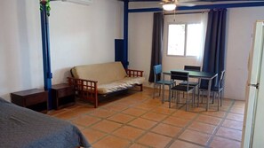 A room with a sofa, a table with chairs, a window with curtains, and a ceiling fan. - Cozy 1-bedroom studio in peaceful Jaco with AC (Jaco)