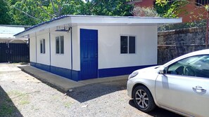 A small, single-story building with a blue door and windows, adjacent to a parked car. - Cozy 1-bedroom studio in peaceful Jaco with AC (Jaco)
