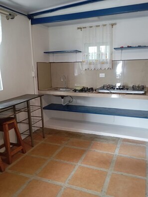 A kitchen with a gas stove, sink, and a window with curtains. - Cozy 1-bedroom studio in peaceful Jaco with AC (Jaco)