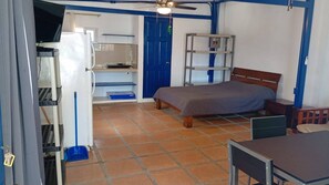 A compact room with a bed, a desk, a chair, a TV, and a blue door. - Cozy 1-bedroom studio in peaceful Jaco with AC (Jaco)