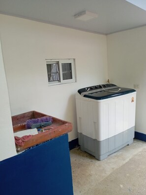 A compact room with a washing machine, a small window, and a blue wall. - Cozy 1-bedroom studio in peaceful Jaco with AC (Jaco)