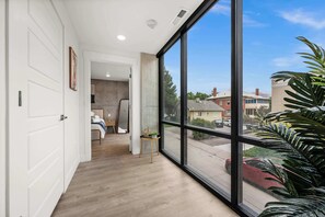 A hallway with a large window, a door, and a bed with a bedside table. - Prime Location Rooftop, Pool, Hot Tub & Gym (Salt Lake City)