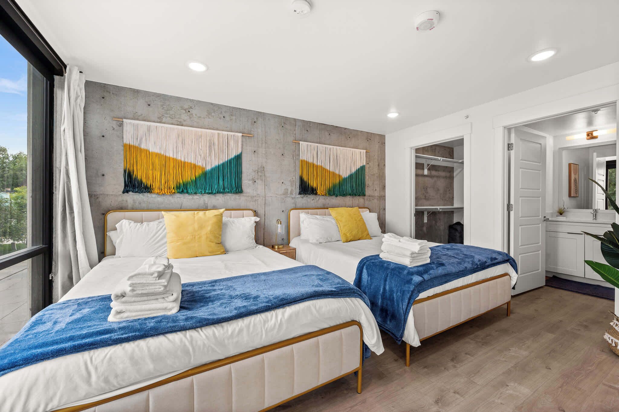 A hotel room with two beds, a large window, a wardrobe, and a bathroom.