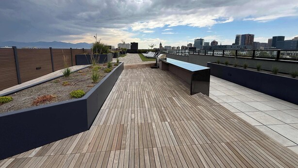 En tagterrasse med en lang træterrasse, grillområde og udsigt over byens skyline.
