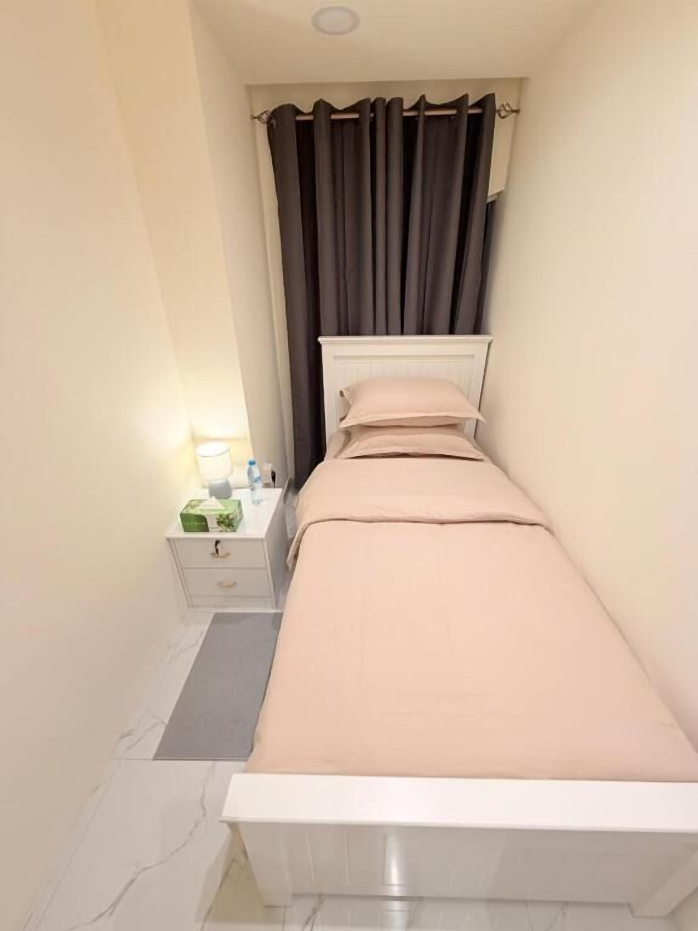 A small, narrow room with a single bed, a nightstand, and a curtain.