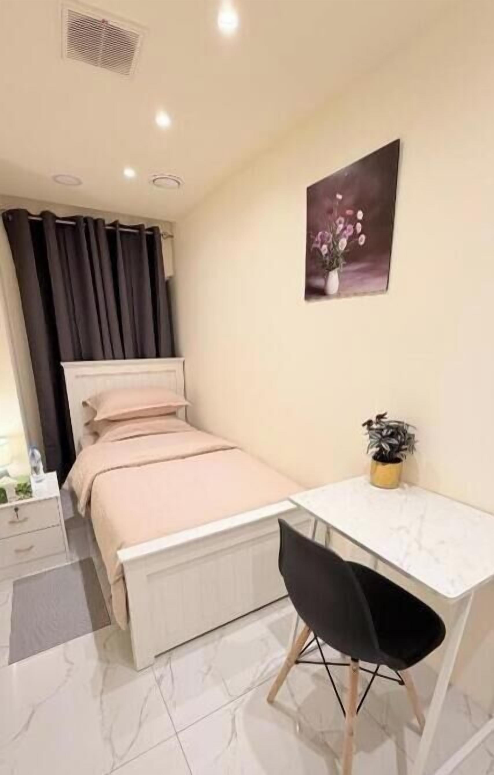 Un dormitorio con cama, mesita de noche, silla y escritorio con planta.