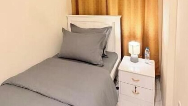 A single bed with a headboard, a bedside table with a lamp, and a curtain.