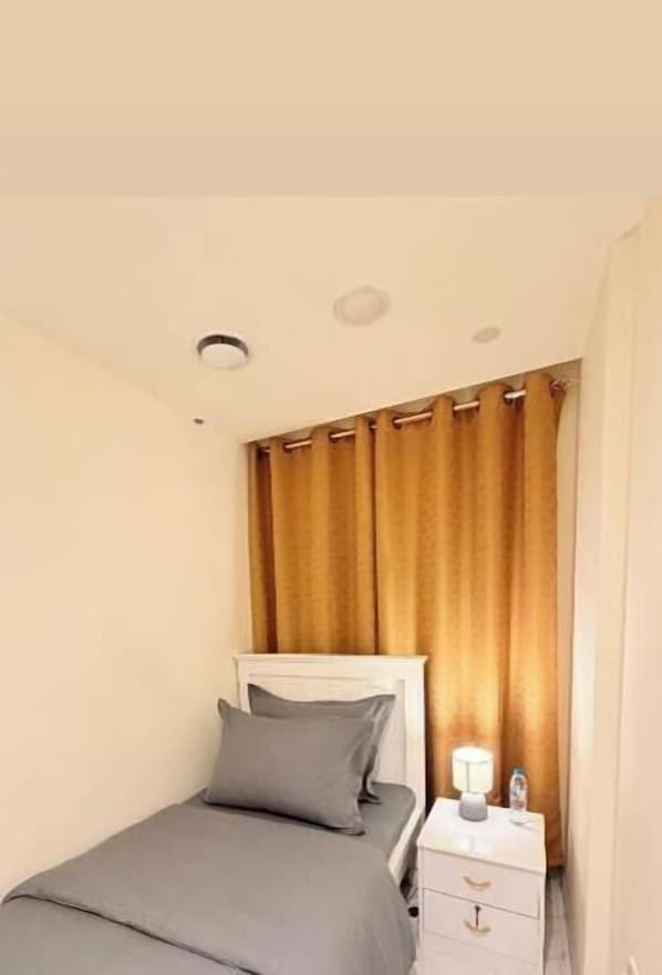 A single bed with a headboard, a bedside table with a lamp, and a curtain.