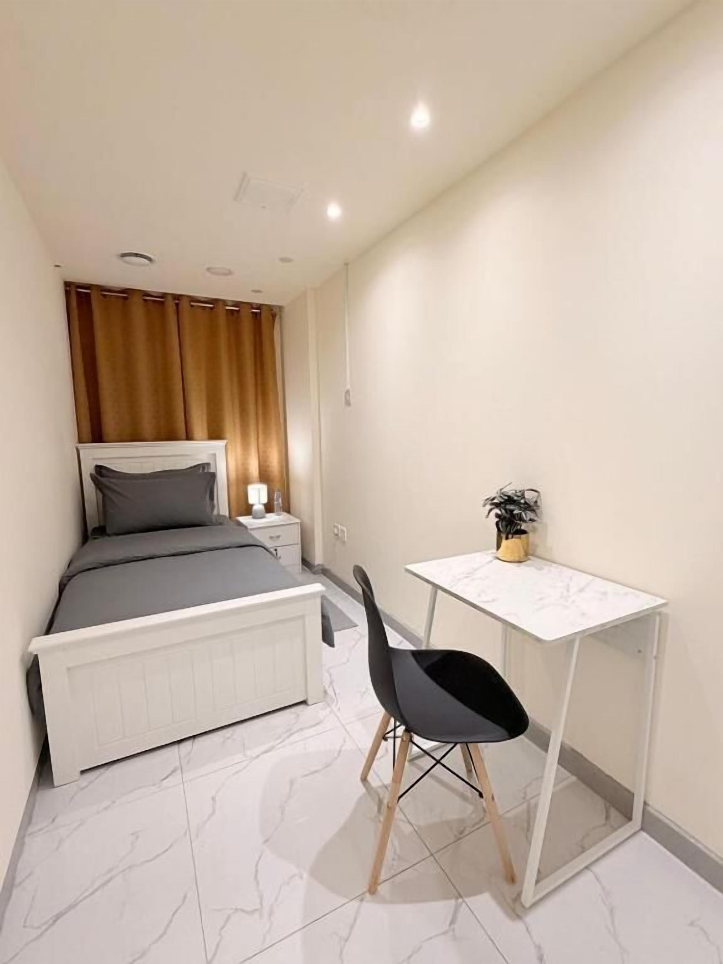 Un dormitorio con cama, mesita de noche, lámpara y un pequeño escritorio con silla.