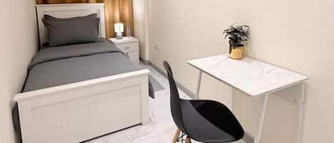A bedroom with a bed, bedside table, lamp, and a small desk with a chair.