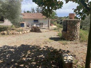 A rustic house with a tiled roof, a stone pillar, and a garden area with a gravel path. - Little House in Provence—The Watering Trough (Flayosc)