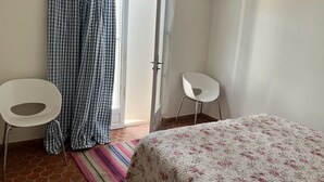 Ein Zimmer mit einem Bett, zwei Stühlen, einer Tür und einem fensterbepflanzten Fenster.