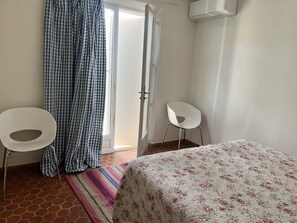 Ein Zimmer mit einem Bett, zwei Stühlen, einer Tür und einem fensterbepflanzten Fenster.