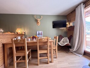 A dining area with a wooden table and chairs, a mounted deer head on the wall, a flat-screen TV, and a window with curtains. - 50m from ski slopes, 2nd floor, swimming pool, balcony, ski locker, 50m², Vars (Vars)
