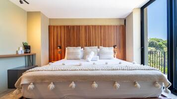 A modern bedroom with a large bed, wooden headboard, and a view of greenery through a balcony.