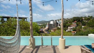 A poolside area with a hammock, lounge chairs, and a view of a coastal town.