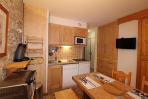 A compact kitchen with wooden cabinets, a microwave, a sink, and a dining table with chairs. - Floor -1, terrace, tv, ski locker, 33m², Aussois (Aussois)