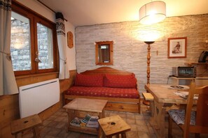 A cozy room with a wooden sofa, a table with magazines, a small wooden stool, a stone wall, and a window with curtains. - Floor -1, terrace, tv, ski locker, 33m², Aussois (Aussois)