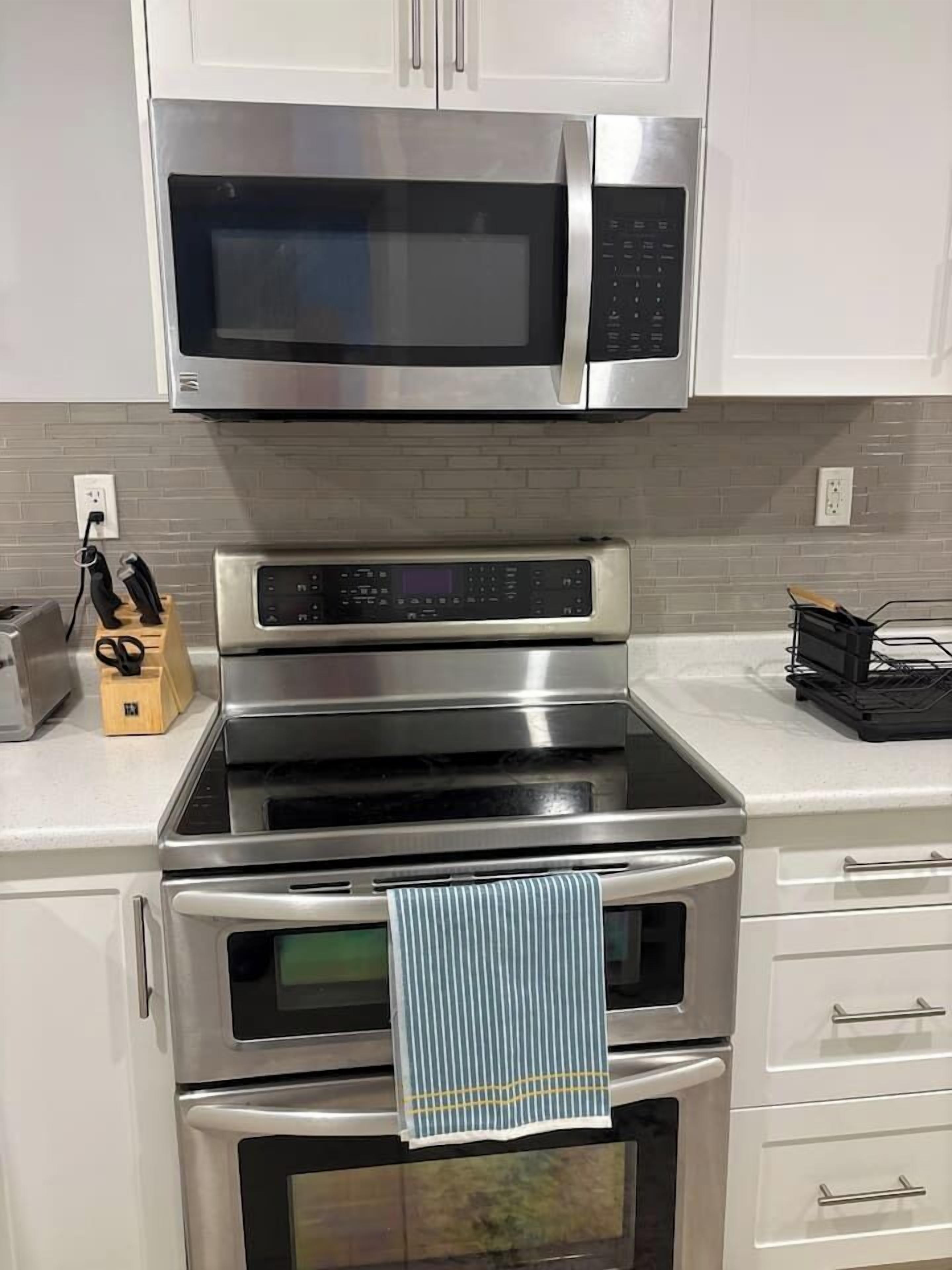 Eine Küche mit Mikrowelle, Backofen und Toaster. Auf der Arbeitsplatte befinden sich ein Messerblock und eine Brotdose.