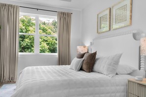 A bedroom with a large bed, a bedside table, a nightstand, a window with curtains, and two wall-mounted picture frames. - Preserve Views | Game Room | Direct Beach Access (Saint Augustine)