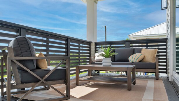 Une terrasse en bois avec un canapé et des fauteuils, une petite table et une plante en pot.