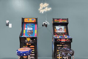Deux bornes d’arcade, l’une pour le jeu Pac-Man et l’autre pour Mortal Kombat, sont placées devant un mur gris orné d’un panneau néon sur lequel on peut lire : « Ensemble, c’est mieux ».