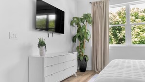 Une chambre à coucher moderne avec un lit, un téléviseur fixé au mur, un radiateur et une fenêtre avec des rideaux.