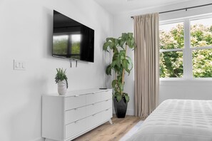 Ein modernes Schlafzimmer mit Bett, einem an der Wand montierten Fernseher, einem Heizkörper und einem Fenster mit Vorhängen.